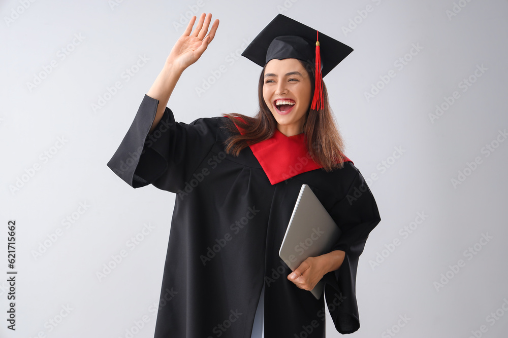 Female graduate student with laptop on light background