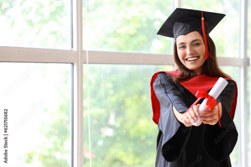 Female graduate student with diploma near window in room