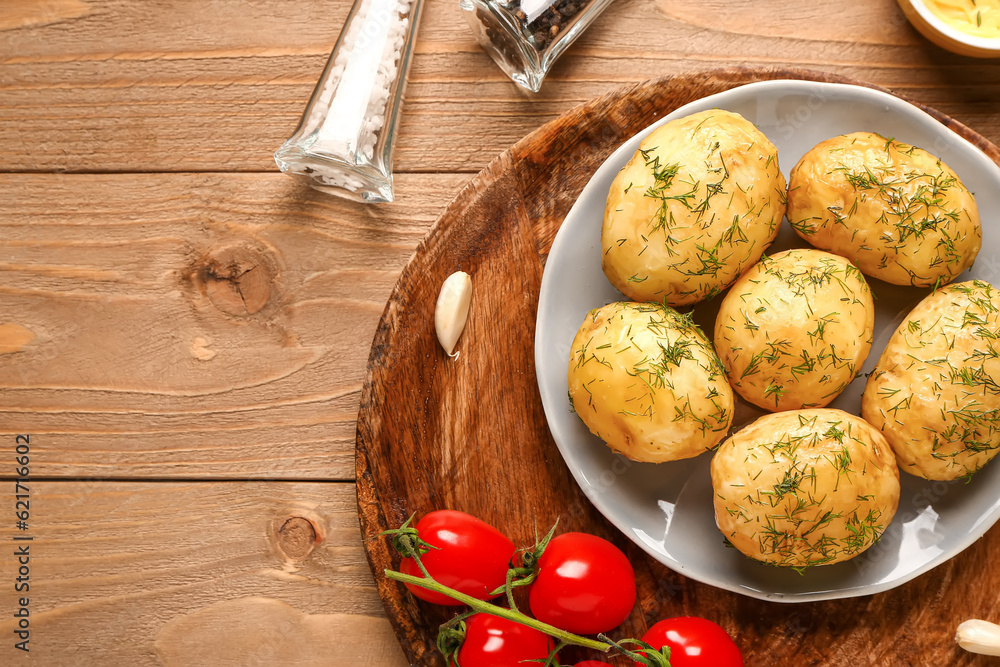 Plate of boiled baby potatoes with dill and tomatoes on wooden background