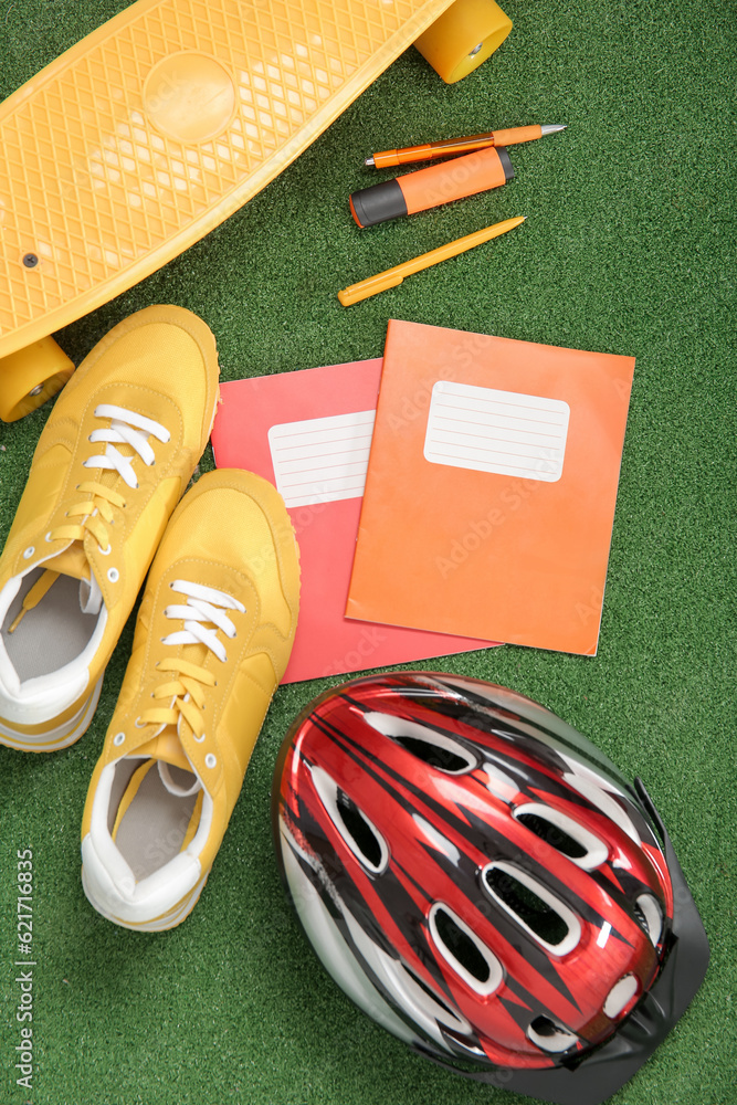 Bike helmet with sneakers, skateboard and different stationery on color background