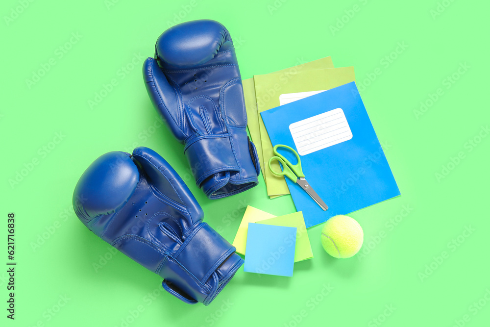 Boxing gloves with tennis ball and different stationery on green background