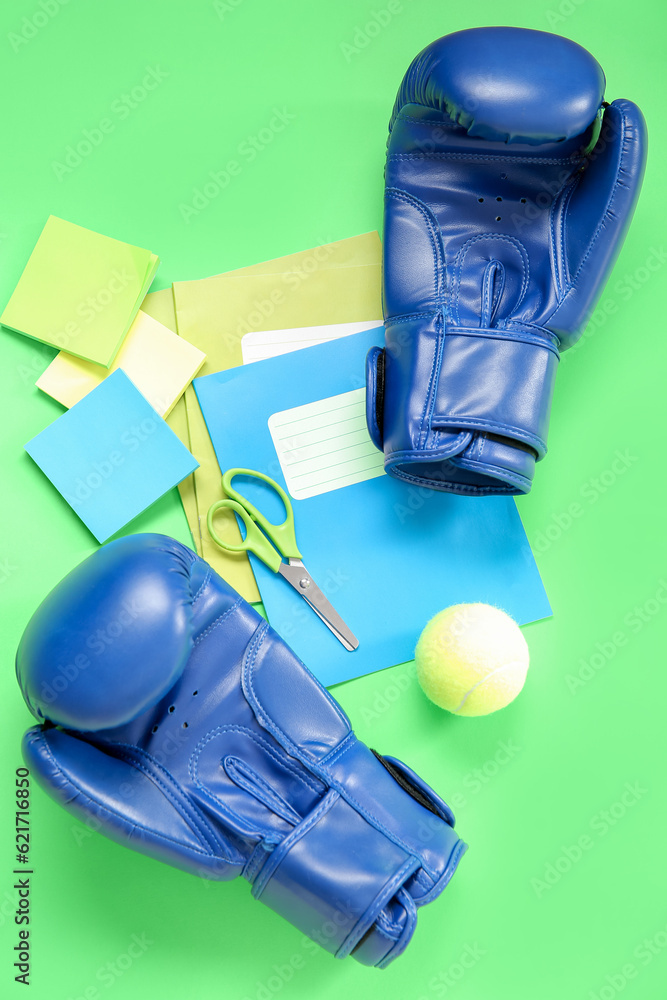 Boxing gloves with tennis ball and different stationery on green background