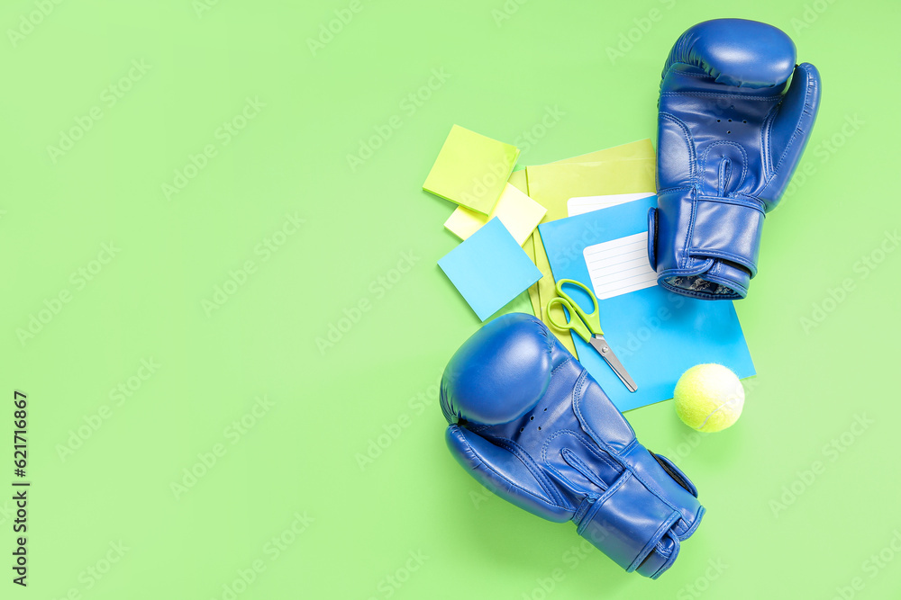 Boxing gloves with tennis ball and different stationery on green background