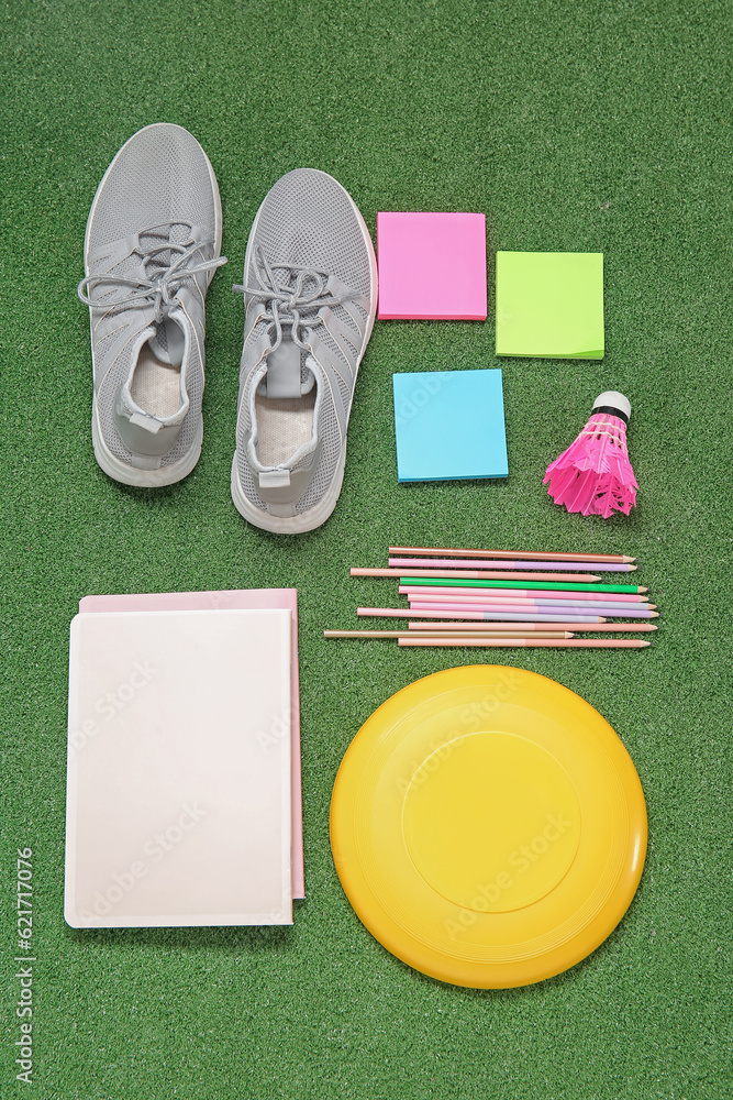 Sneakers with frisbee disk, badminton shuttlecock and different stationery on color background