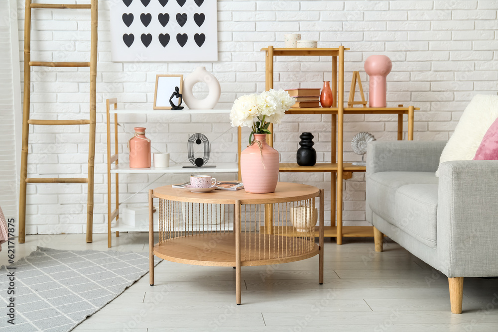 Vase of white peonies on coffee table, couch and shelving unit near white brick wall