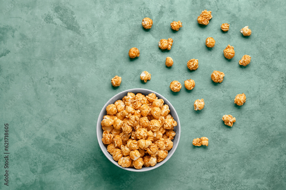 Bowl with tasty popcorn on green background