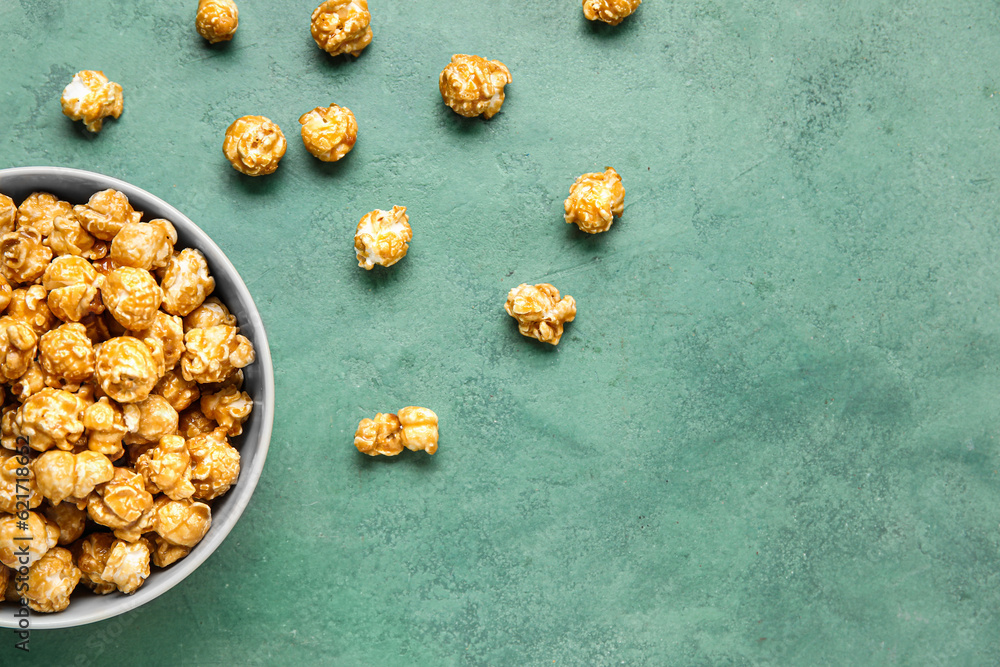 Bowl with tasty popcorn on green background