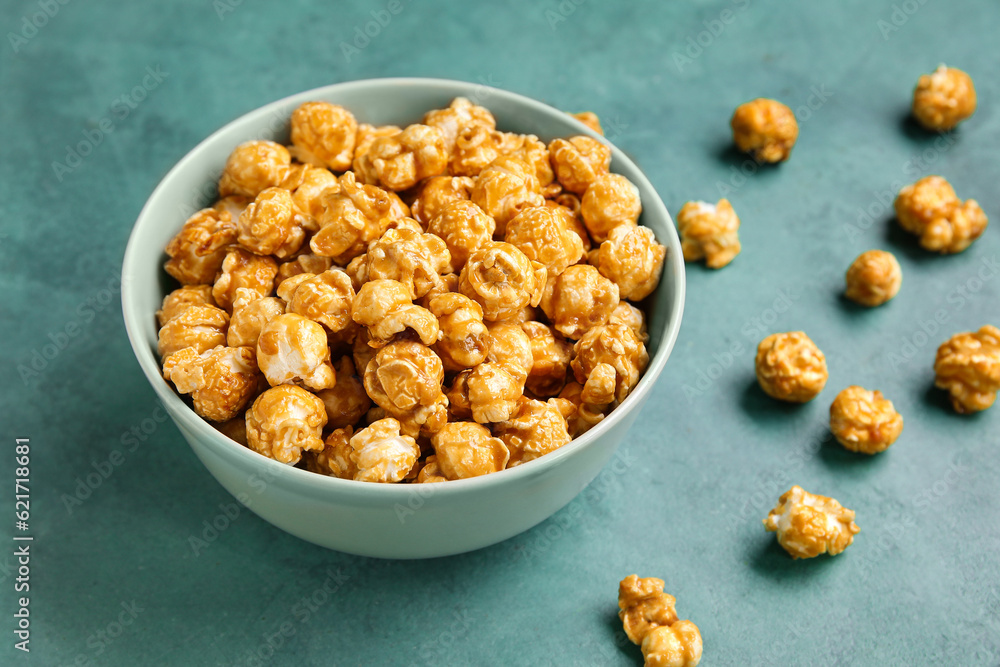 Bowl with tasty popcorn on green background