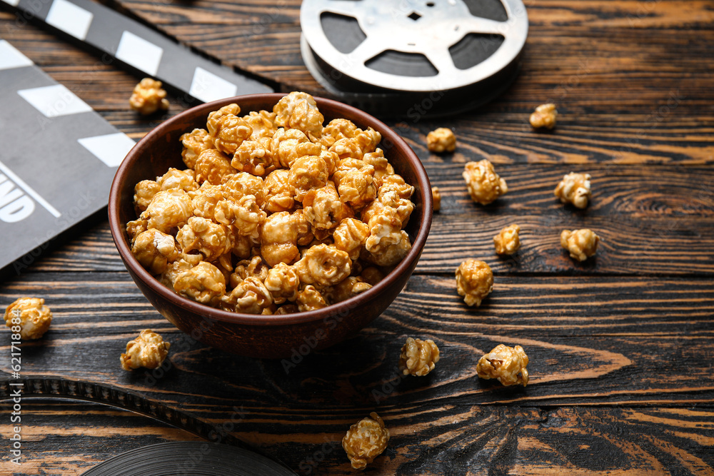 Bowl with tasty popcorn, clapperboard and film reel on wooden background