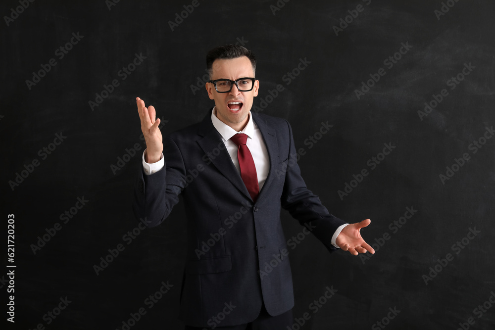 Angry male teacher near blackboard in classroom