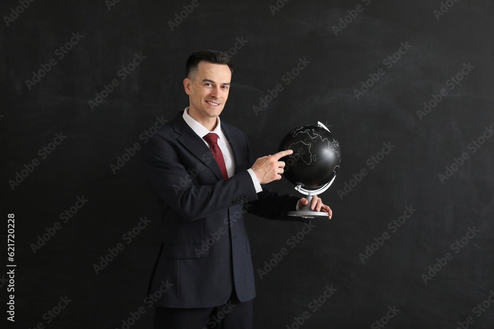 Male Geography teacher with globe near blackboard in classroom