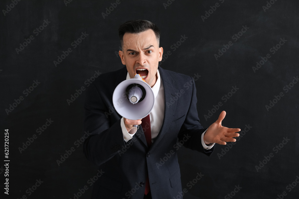 Angry male teacher shouting into megaphone near blackboard in classroom