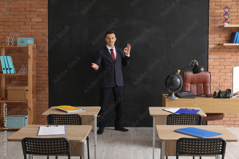 Male teacher showing OK near blackboard in classroom