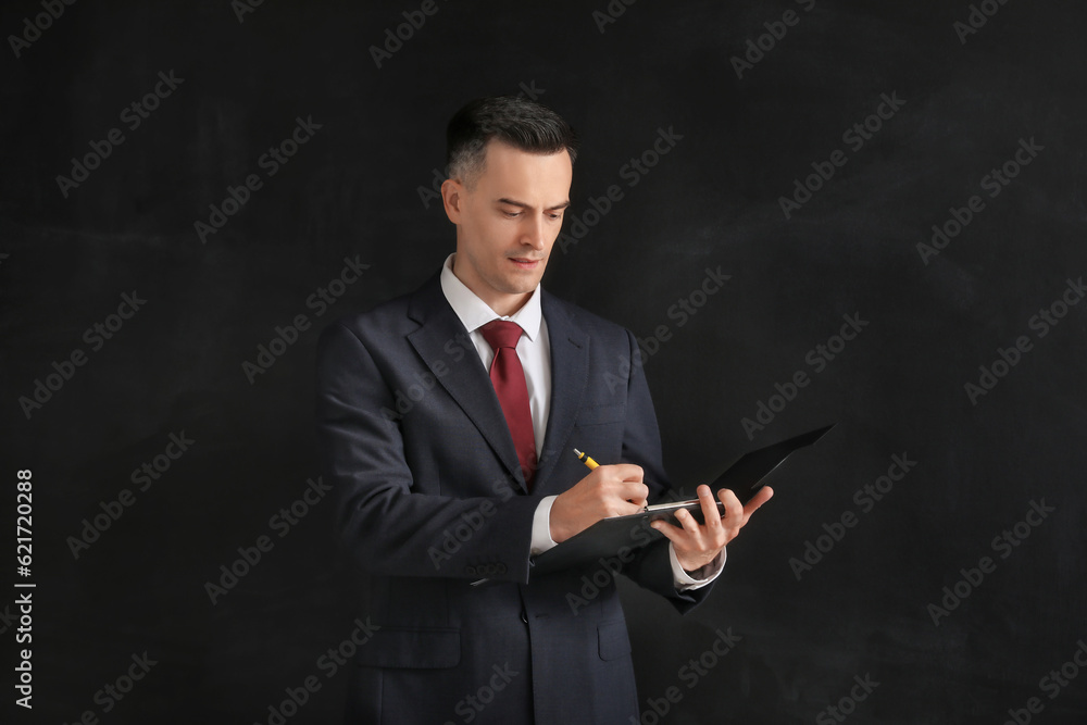 Male teacher writing in clipboard near blackboard in classroom