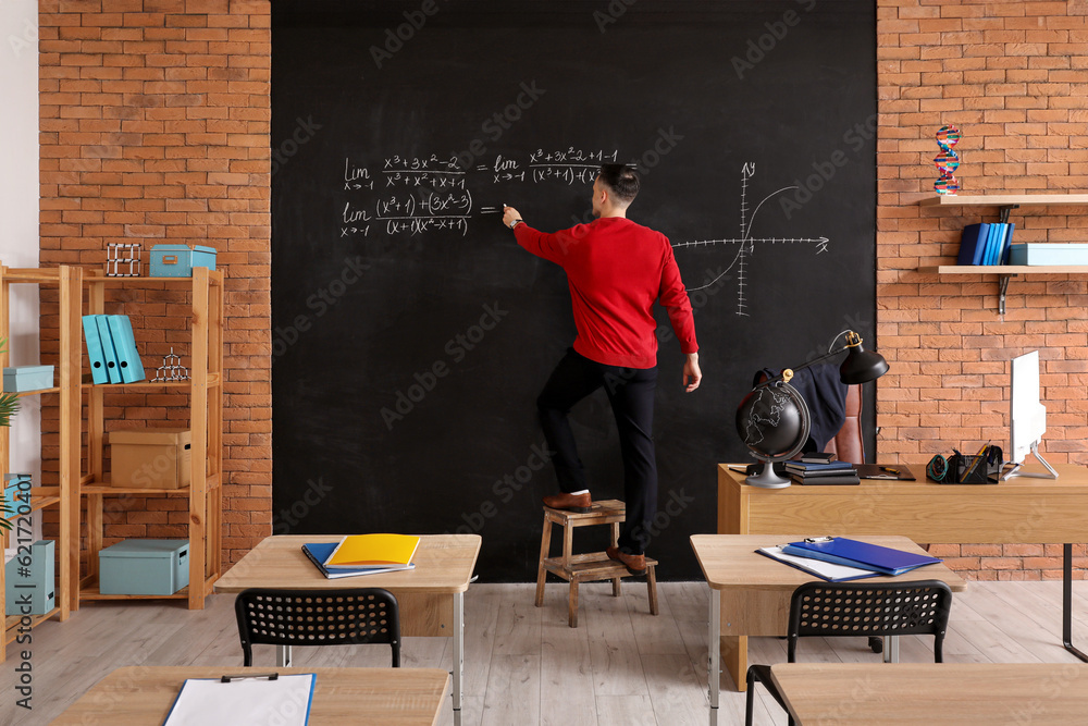 Male Math teacher writing equation on blackboard in classroom