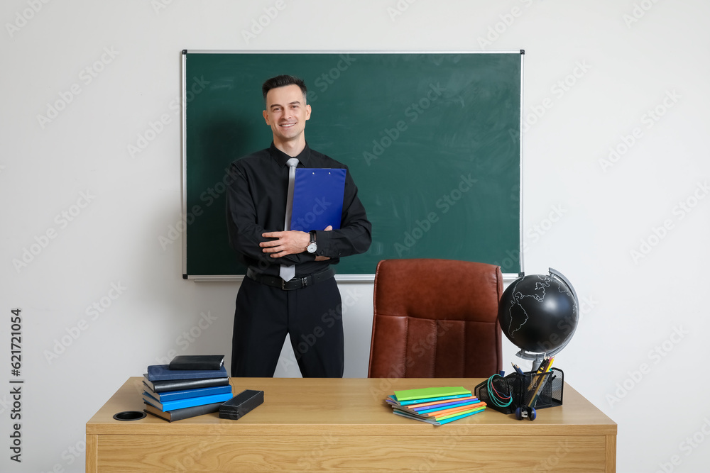 Male teacher with clipboard near chalkboard in classroom