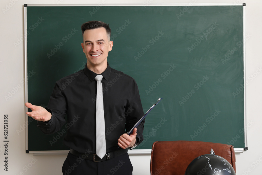 Male teacher with clipboard near chalkboard in classroom