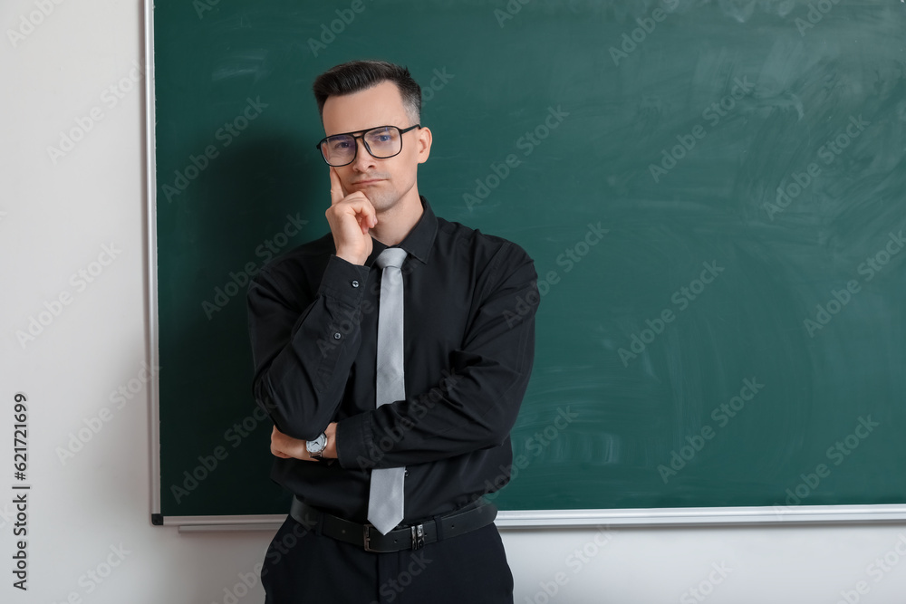 Thoughtful male teacher near chalkboard in classroom