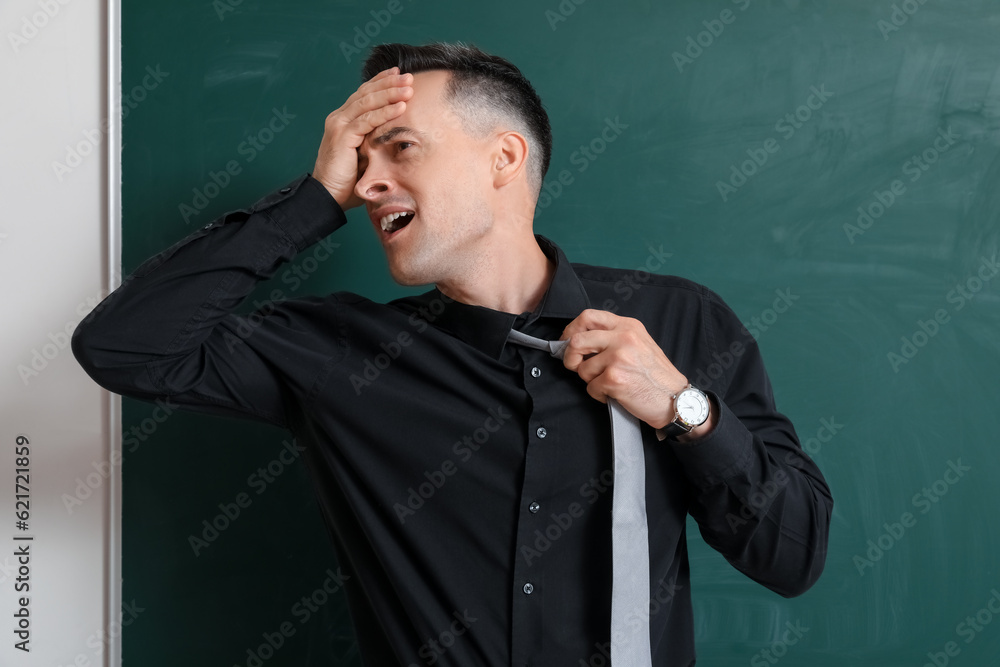 Stressed male teacher near chalkboard in classroom