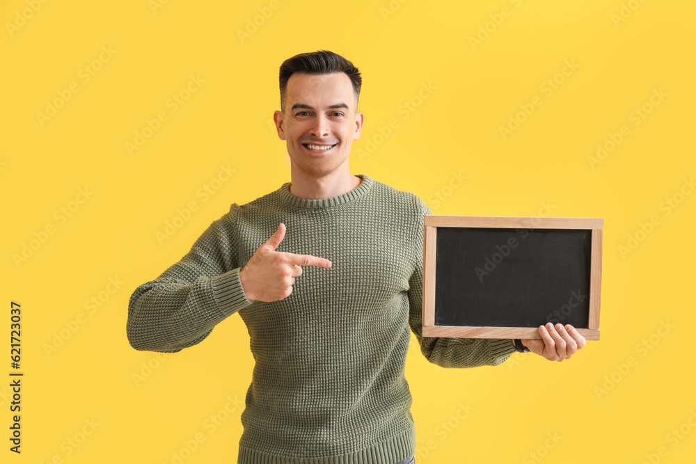 Male teacher pointing at chalkboard on yellow background