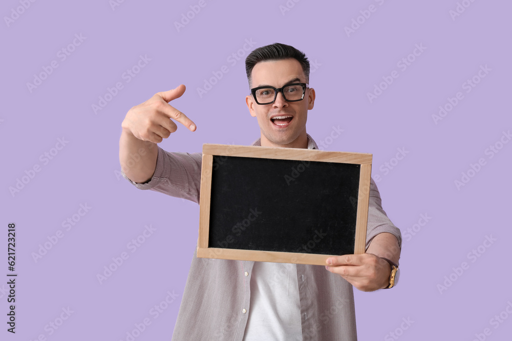 Male teacher pointing at chalkboard on lilac background