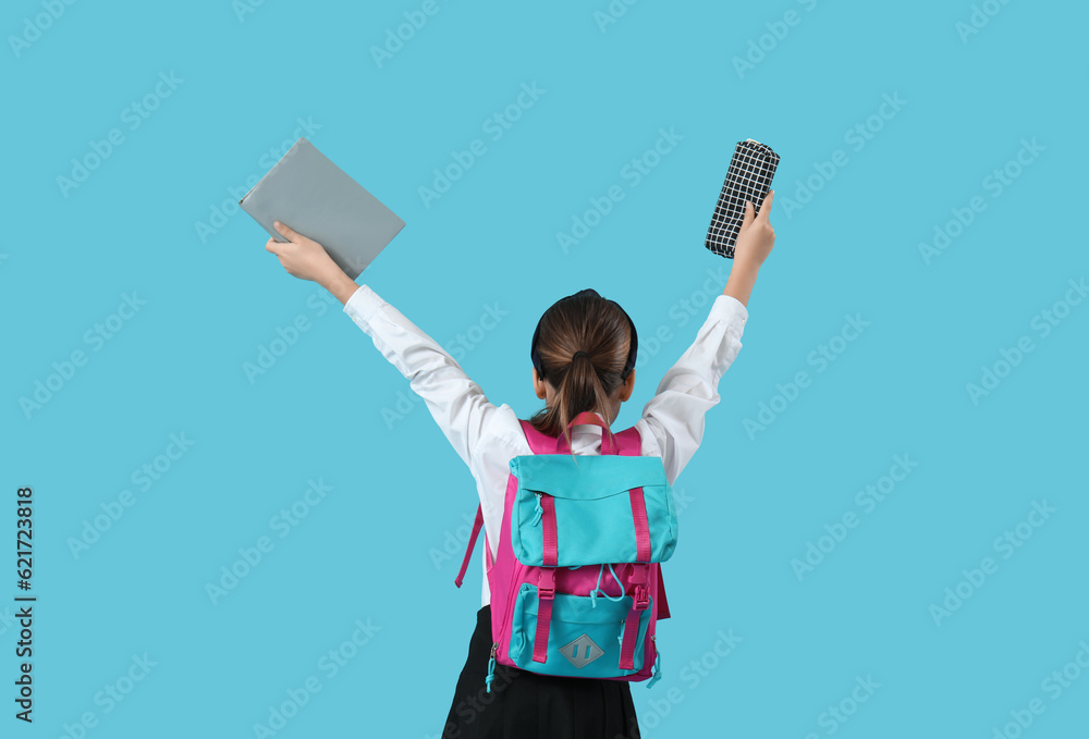 Little schoolgirl with backpack, pencil case and book on blue background, back view