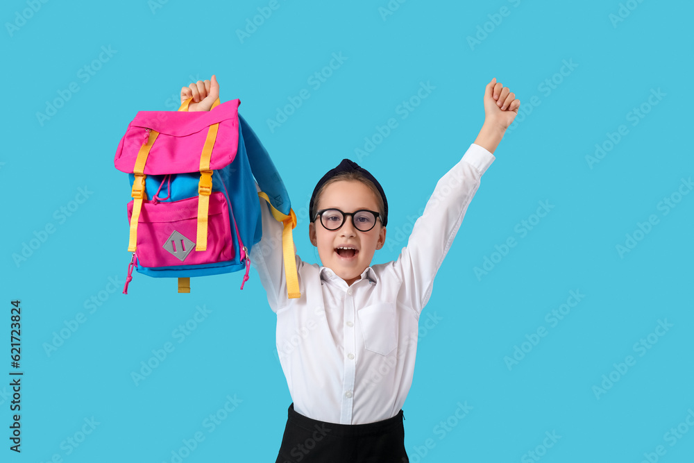 Little schoolgirl with backpack on blue background