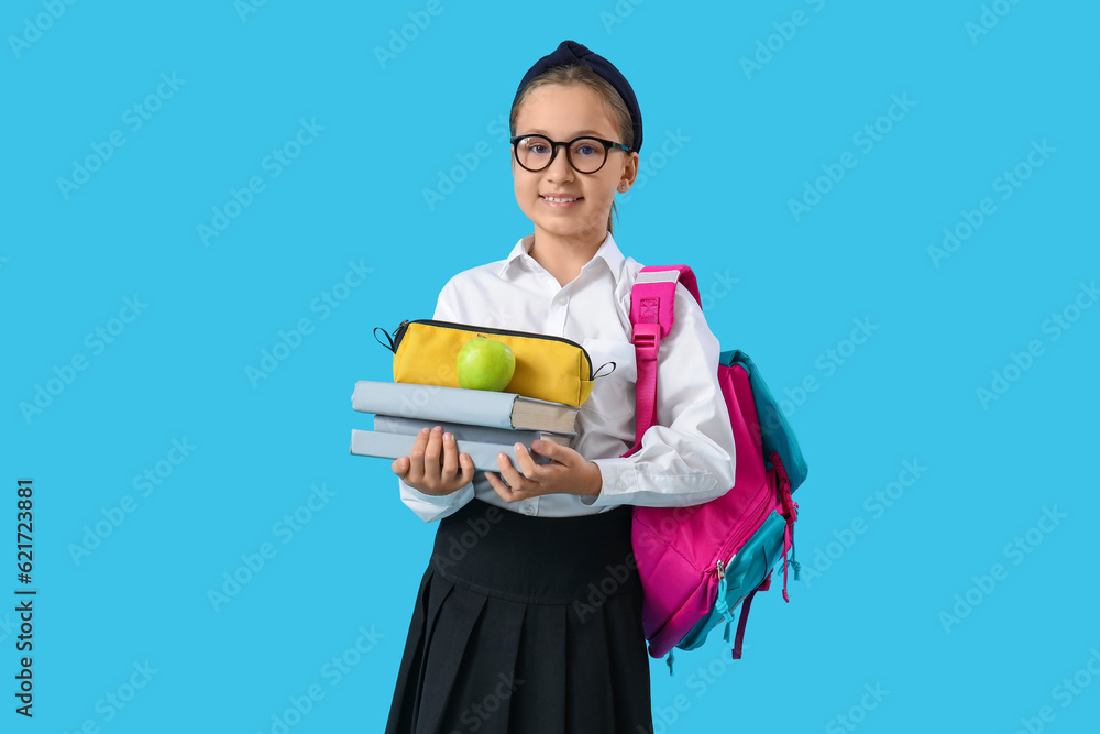 Little schoolgirl with backpack, pencil case and books on blue background