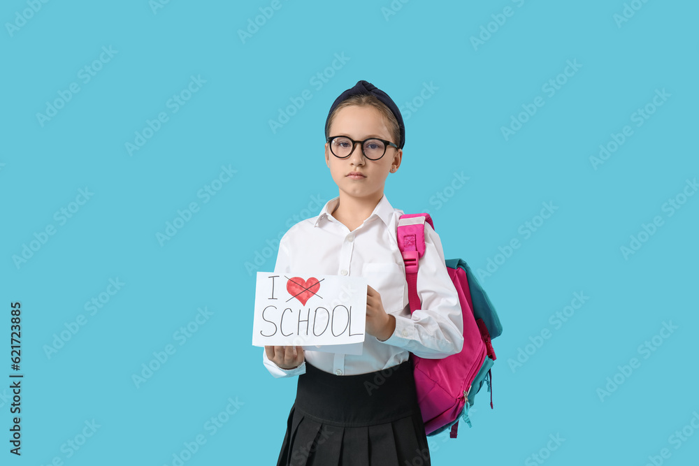 Little schoolgirl holding paper with text I DO NOT LOVE SCHOOL on blue background