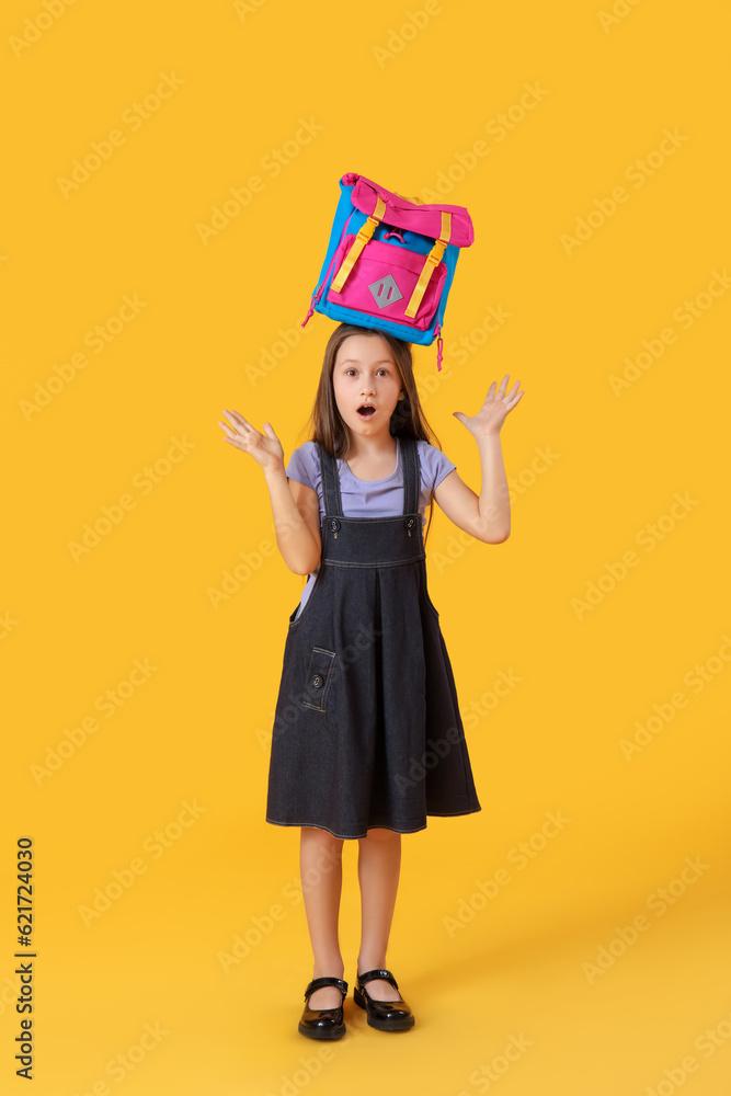 Shocked little girl with backpack on yellow background