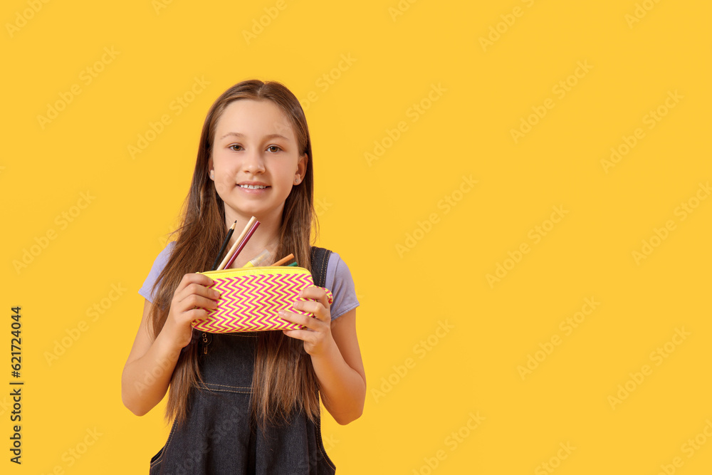 Little girl with pencil case on yellow background