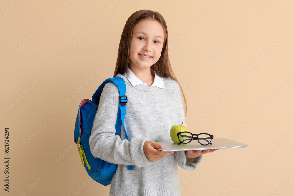 Little schoolgirl with laptop, apple and eyeglasses on beige background