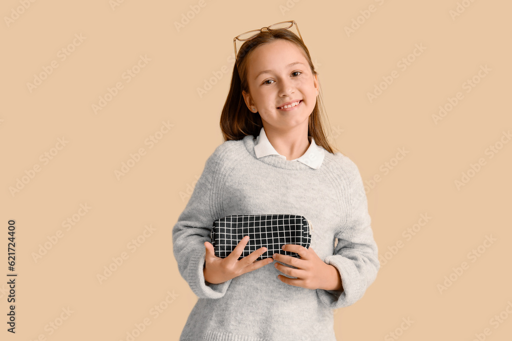 Little girl with pencil case on beige background