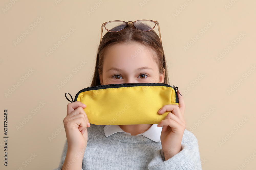 Little girl with pencil case on beige background, closeup