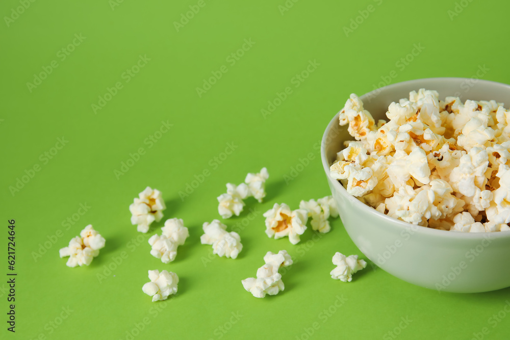 Bowl with tasty popcorn on green background