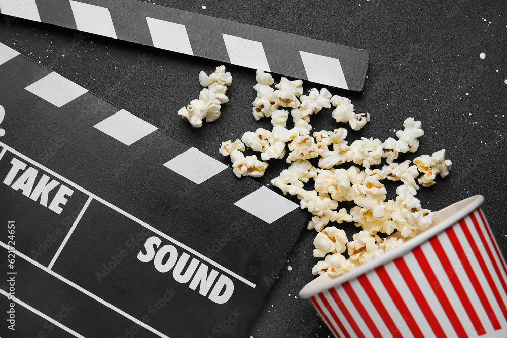 Bucket with tasty popcorn and clapperboard on black background