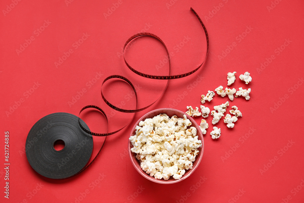 Bowl with tasty popcorn and film reel on red background