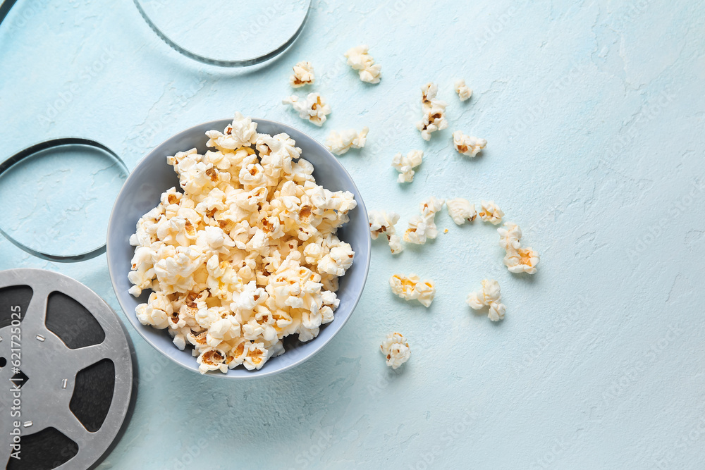 Bowl with tasty popcorn and film reel on blue background