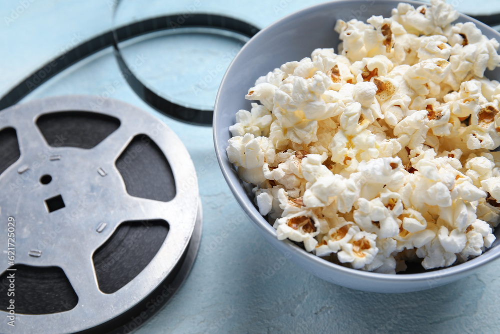 Bowl with tasty popcorn and film reel on blue background