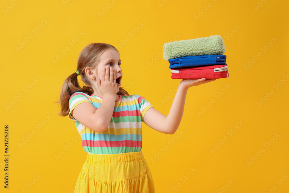 Shocked little girl with pencil cases on yellow background