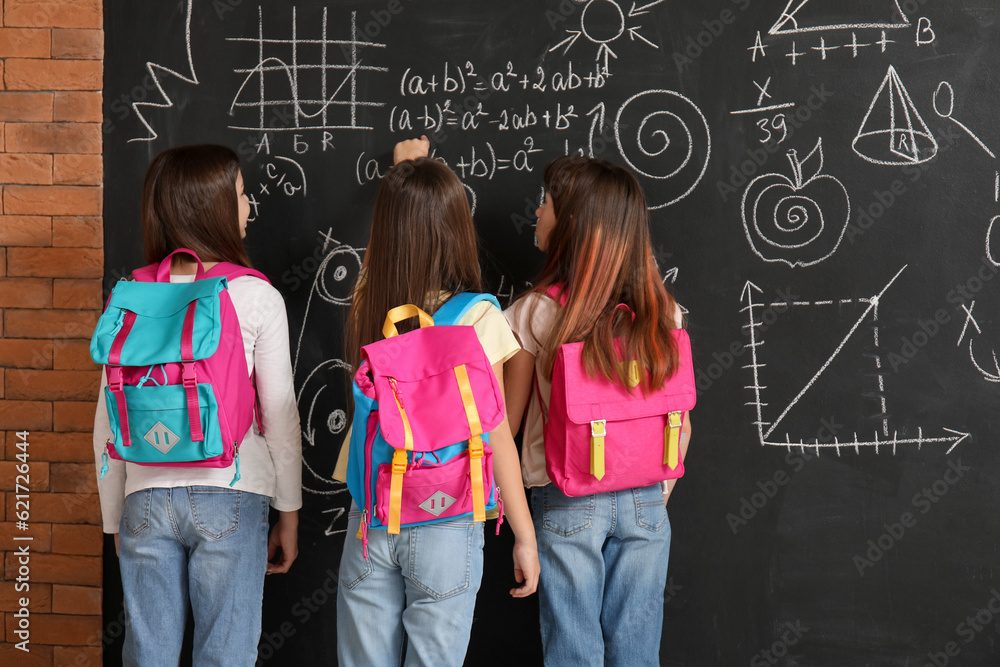 Little girls with backpacks near blackboard, back view