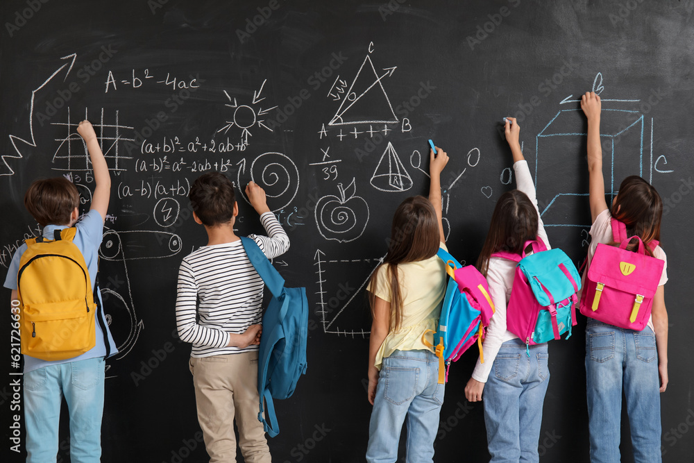 Little pupils with backpacks near blackboard, back view