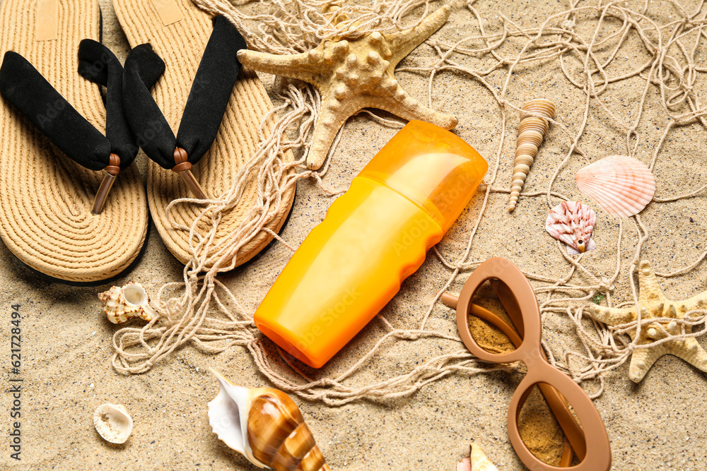 Sunglasses with flip flops, net and bottle of sunscreen cream on sand