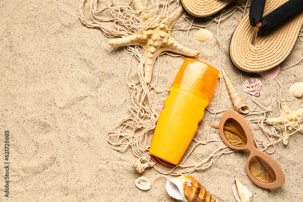 Sunglasses with flip flops, net and bottle of sunscreen cream on sand