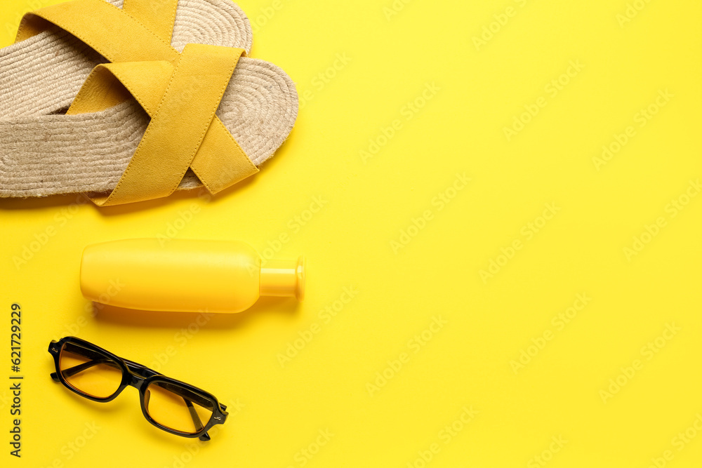 Sunglasses with bottle of sunscreen cream and flip flops on yellow background