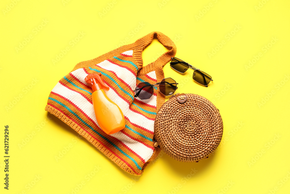 Sunglasses with wicker bag, bikini bra and bottle of sunscreen cream on yellow background