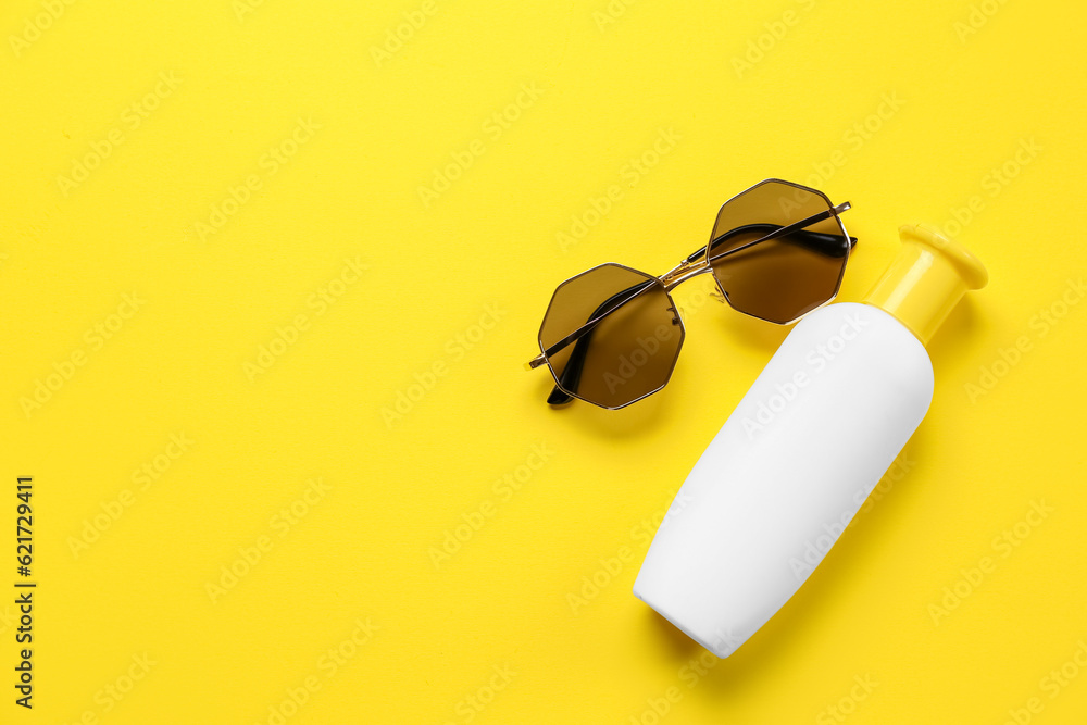 Sunglasses with bottle of sunscreen cream on yellow background