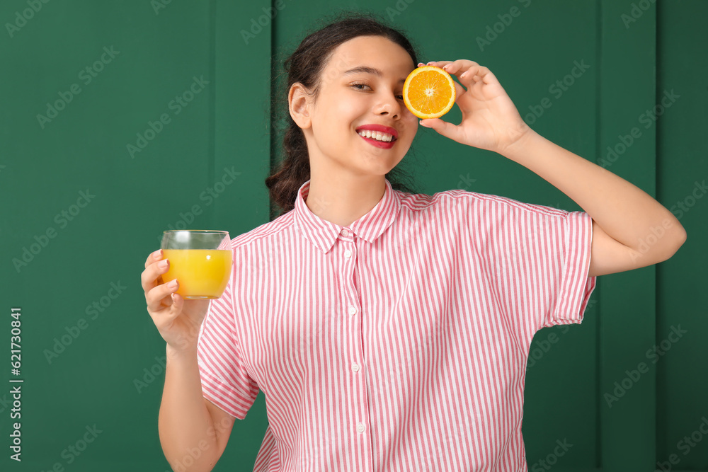 Teenage girl with glass of juice and orange on green background