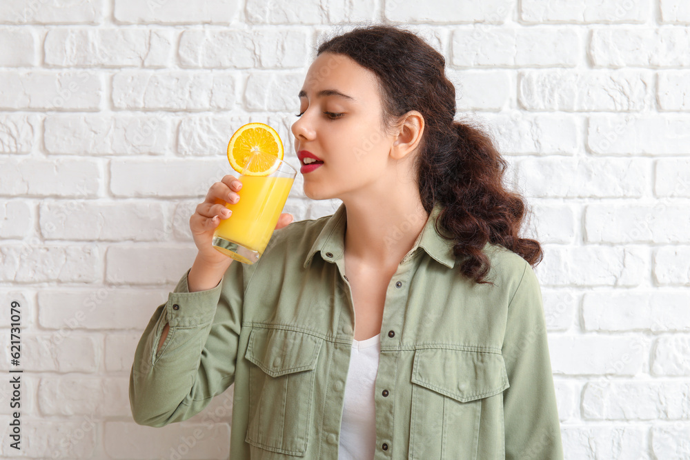 Teenage girl with glass of orange juice on white brick background