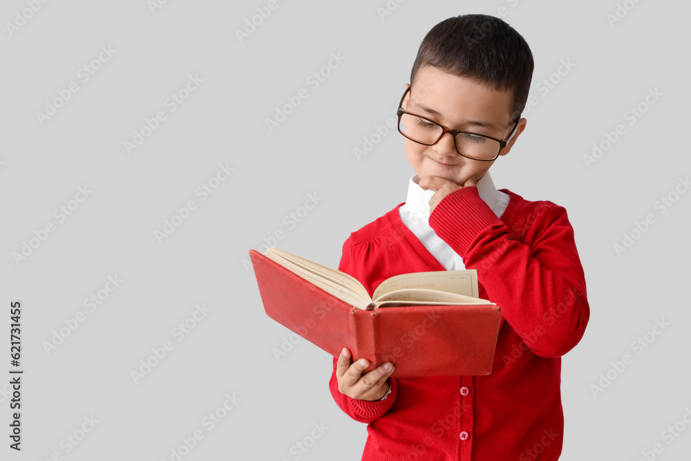 Little schoolboy with book on grey background